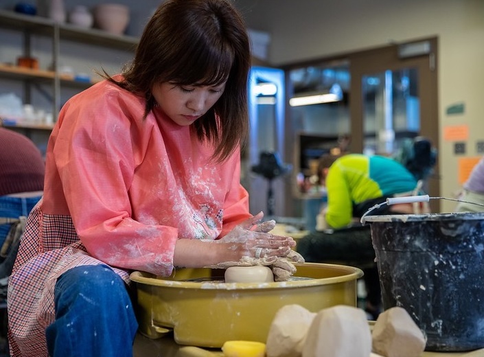 Female student of Asian descent creates a piece of pottery out of clay. 