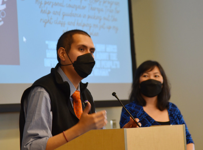 Diego Epinoza is standing at a podium wearing a black face mask at an event for Mission College.