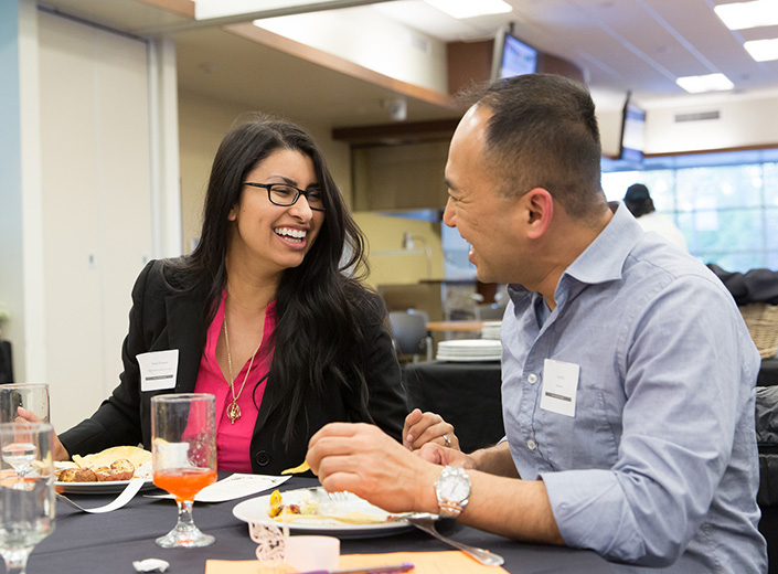 Two career education students chat at an event in their business casual clothes with nametags.