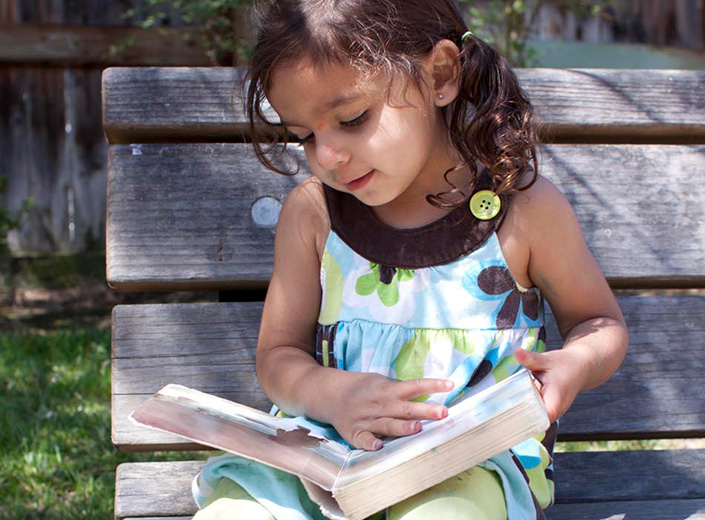 Little girl reading a book on a bench.