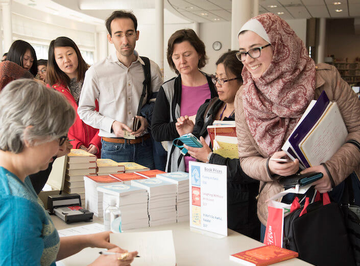 Smiling female student in a hijab gets her copy of a book signed at a book reading event on campus. A line of students waits for their turn.