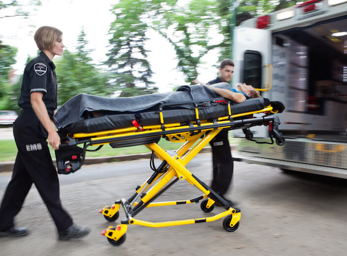 Paramedics wheel a person on a strecher toward an ambulance.