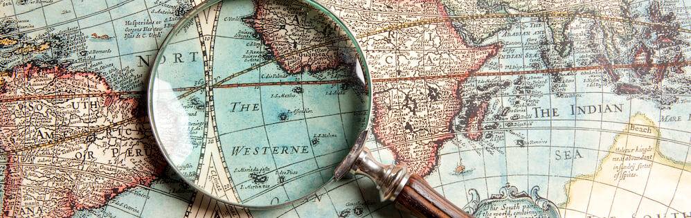 Magnifying glass on aged-looking print map of world.