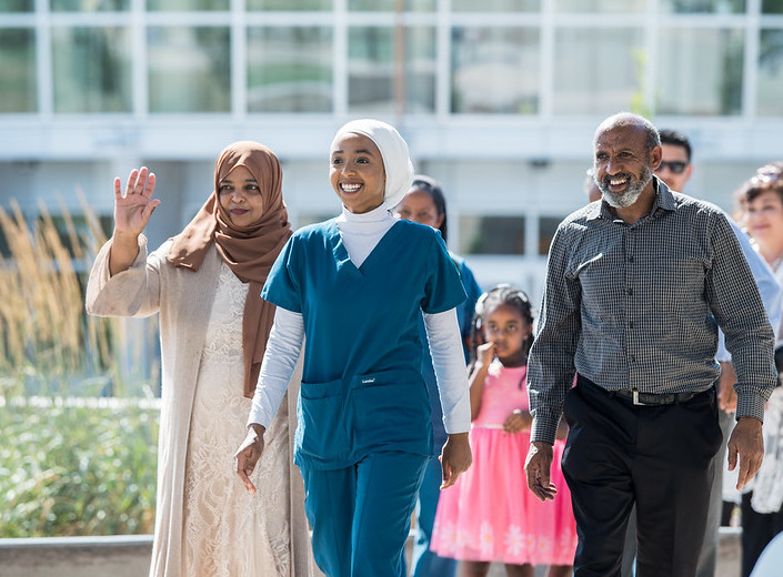 Nursing  graduate in scrubs and white headscarf walks with her family on graduation day.