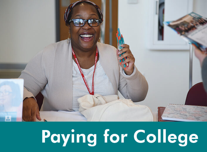 An African-American woman with glasses holds up a handful of pens and smiles wide for the camera. She is seated a table. "Pay for college is written in white across a teal bar on the bottom of the picture.