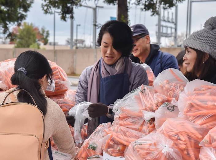 Woman distributes carrots at a food bank.