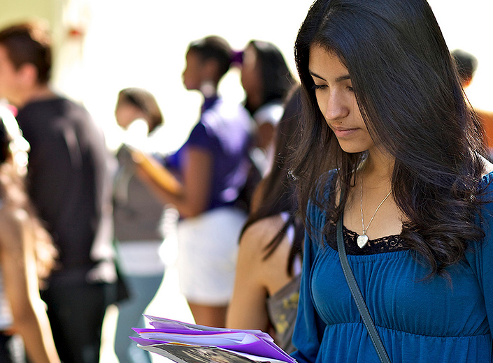 Latinx female student in blue shirt reviews some information in a brochure.