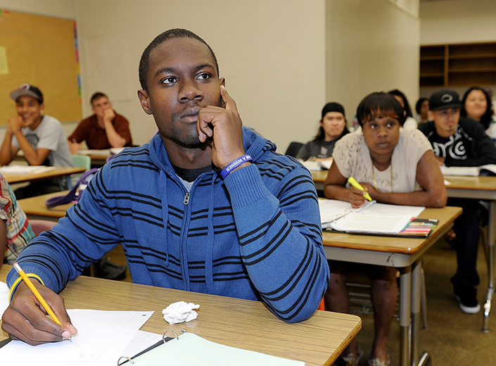 Black male student focuses in a college classroom with a pencil in hand, taking notes.