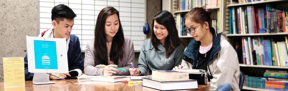 Four students of Asian descent work at a table in the library.
