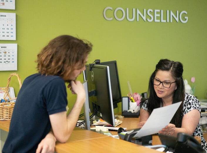 A dark-haired woman in glasses assists a male student in the Counseling Center. 