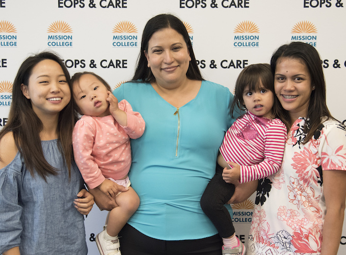 Family of mom and four girls posing for photo in front of "EOPS/CARE" step-and-repeat.