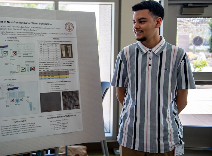 Male Latino student looks at poster board research project. 